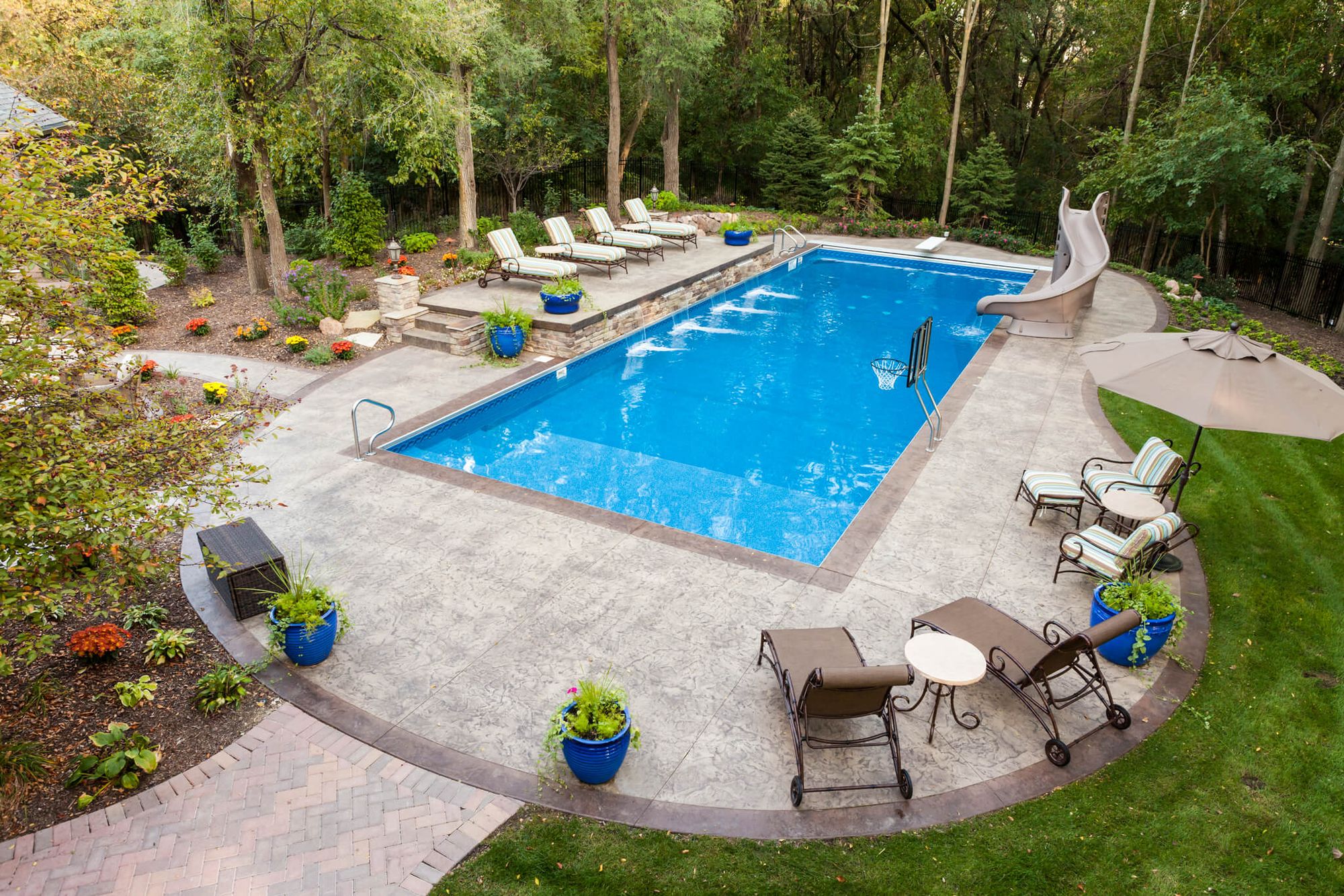 Aerial view of a finished backyard pool with a brick-bordered patio, loungers and lawn