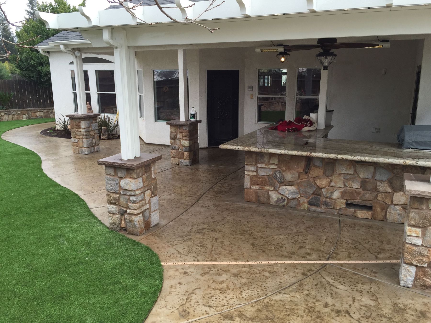 Covered patio with a stone outdoor kitchen and bar beside artificial turf