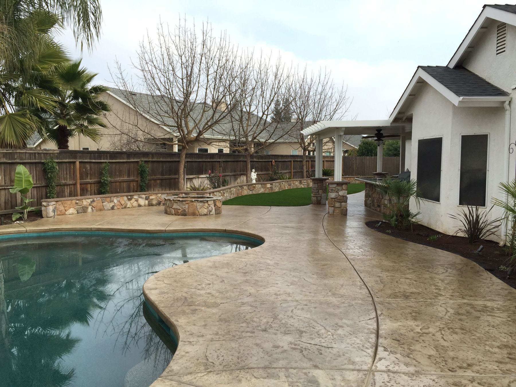Freeform pool with a stamped concrete deck, stone seat wall and covered patio