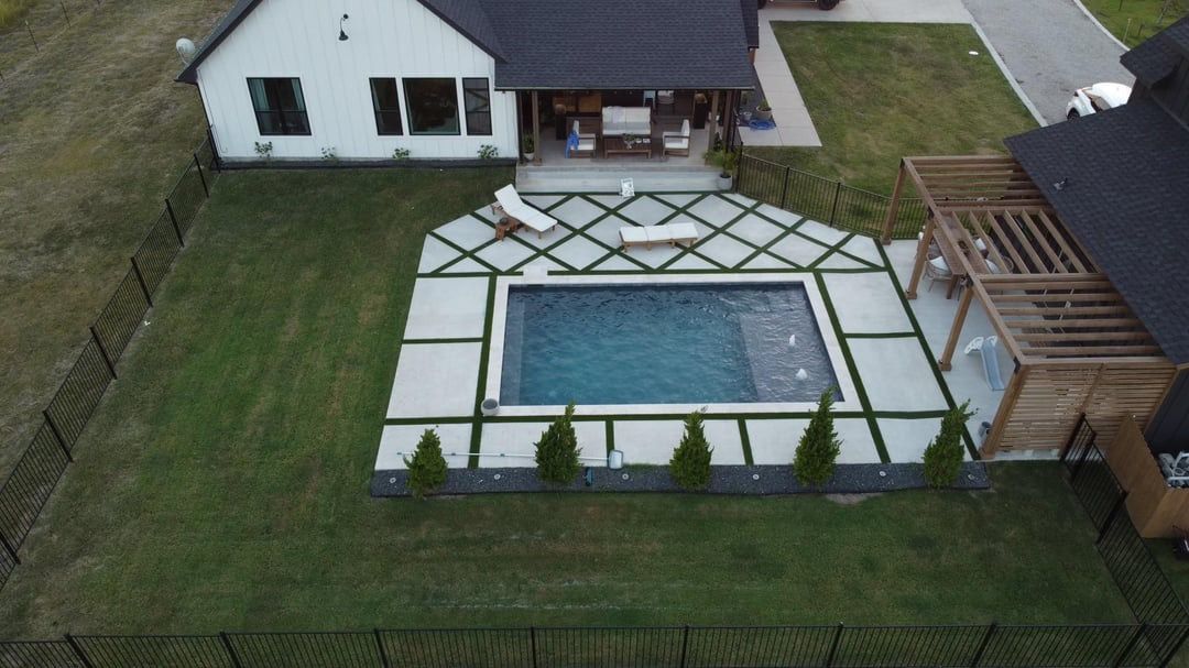 Aerial view of a finished backyard with a paver and turf grid around a pool and a cedar pergola